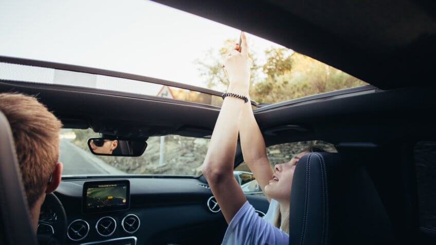 girl taking photo out of sun roof in car