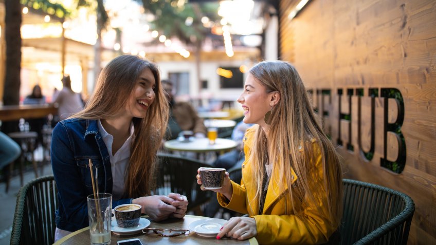 Beautiful , young female friends gossiping while drinking coffee on spring day , outdoor in cafe.