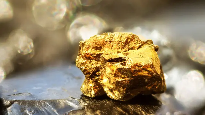 Golden bar on raw coal nuggets with soft focus and shiny background.