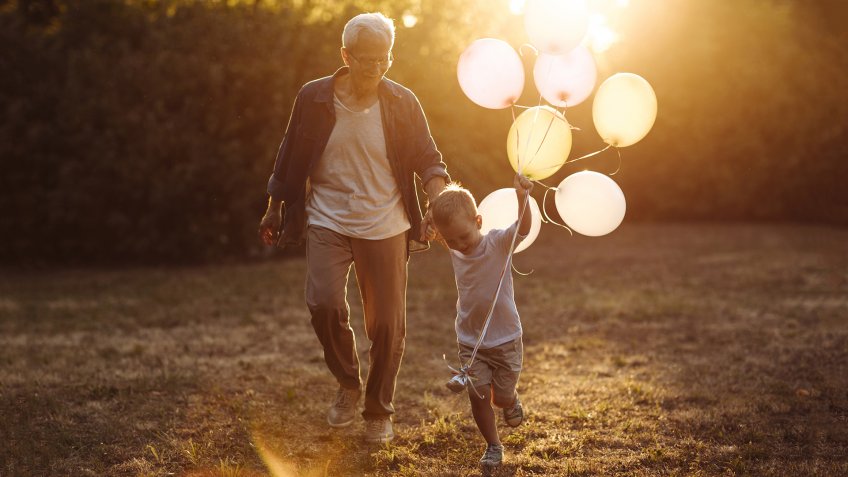 Young boy having fun with grandpa on a sunny day outdoors holding lots of balloons.