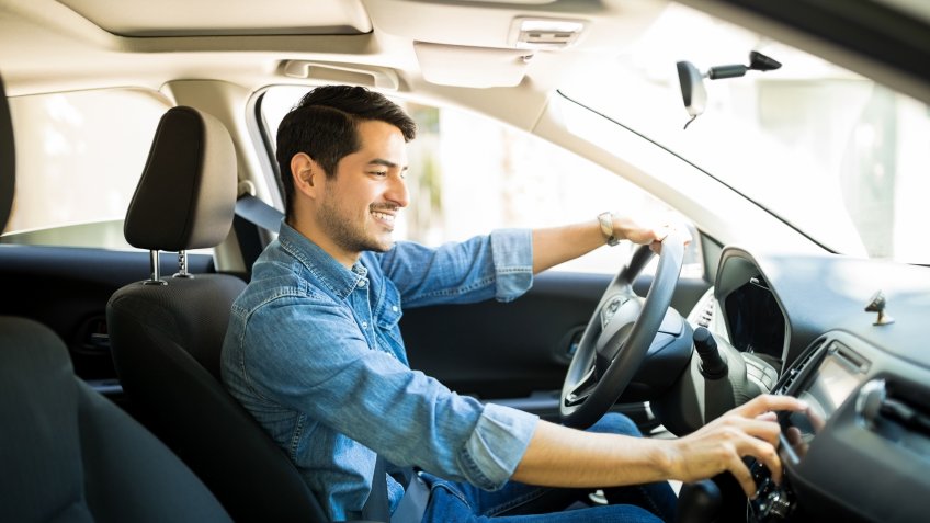 Handsome young man in denim shirt pressing touchscreen on car multimedia panel, switching shifting radio station.
