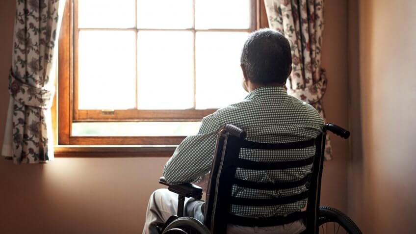 Rearview shot of a senior man looking out the window while sitting in his wheelchair.