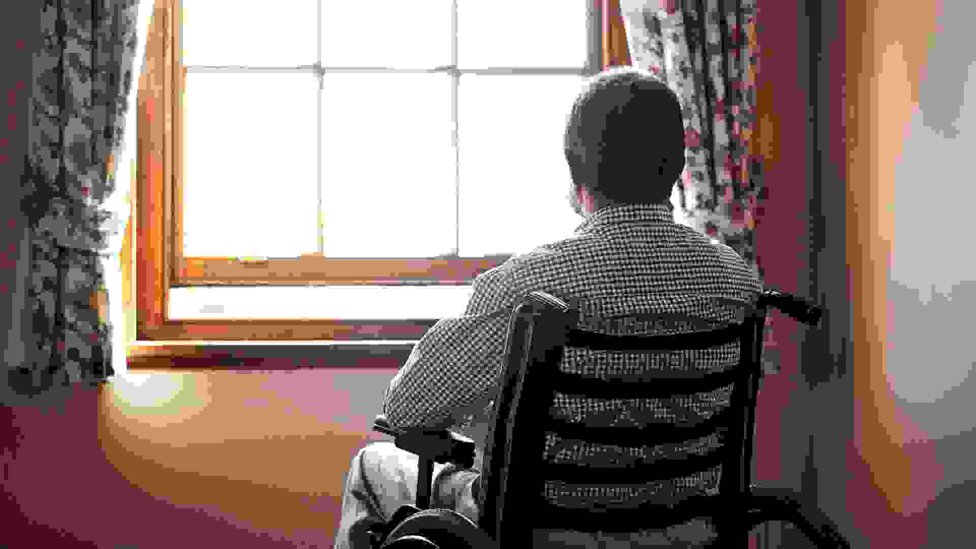 Rearview shot of a senior man looking out the window while sitting in his wheelchair.