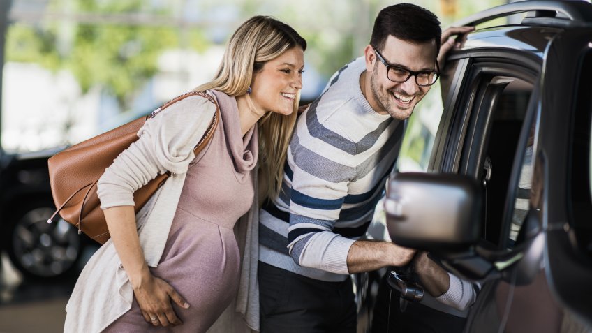 Happy expecting couple searching for the right family car in a showroom.