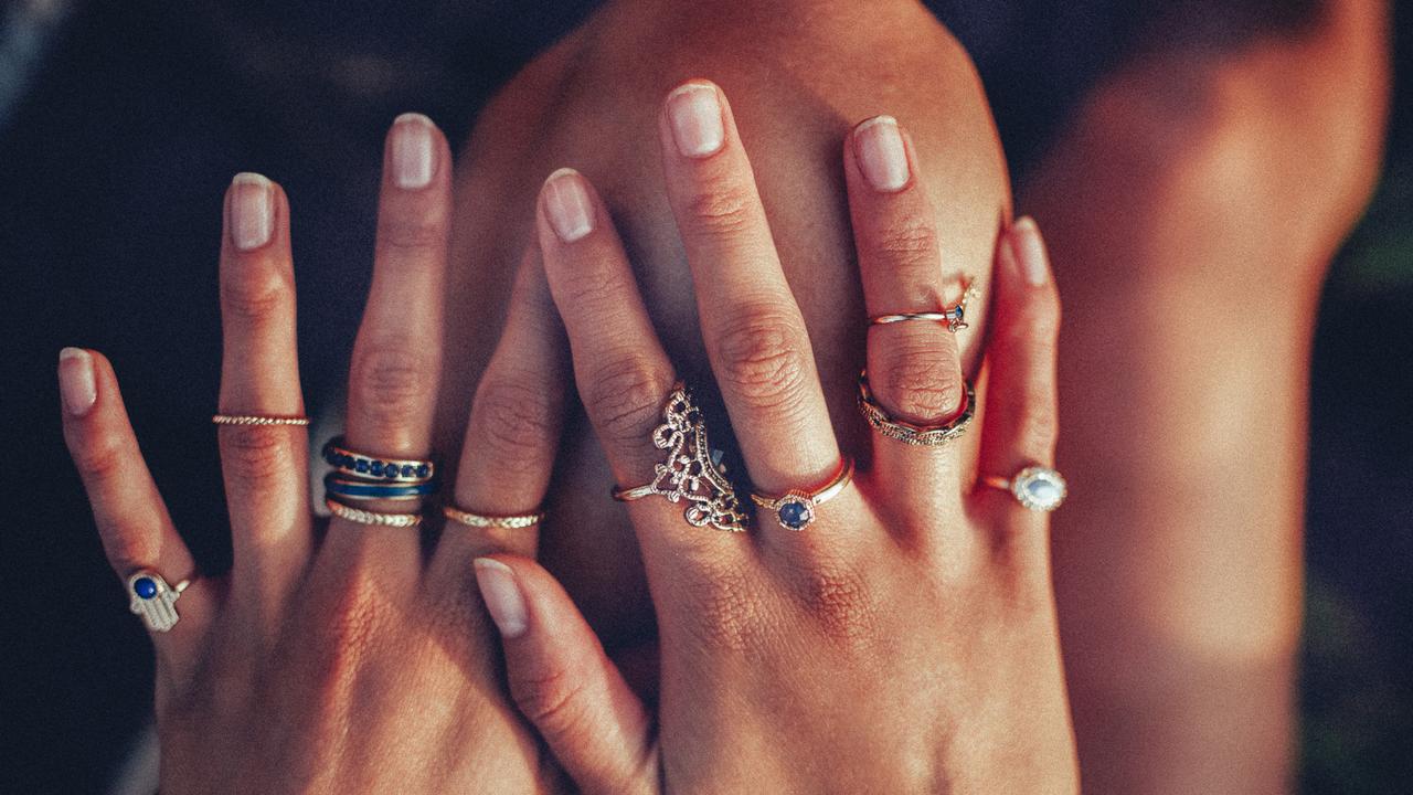 Cropped closeup of a boho girl's hands with many rings on her fingers, in gold and silver with dark blue stones.