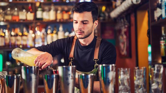 Young bartender at bar counter preparing a cocktail.