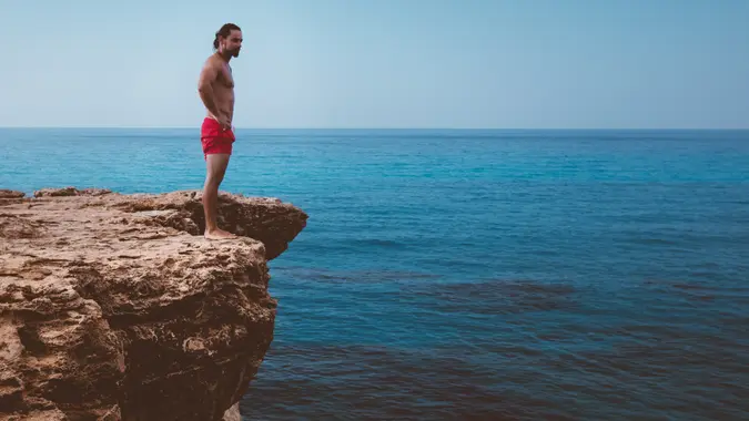 Young active diver standing on cliff looking at sea and preparing to dive into ocean.