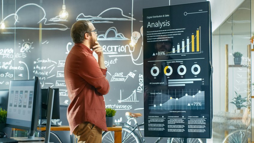 Marketer Looks at Interactive Touchscreen Whiteboard Showing Latest Graphs and Charts on Statistical Growth.