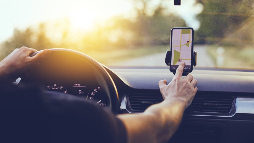 Driver using GPS navigation in mobile phone while driving car at sunset.
