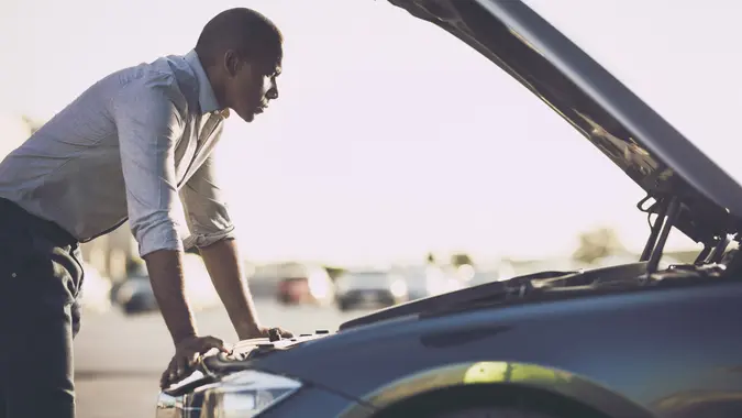 Mid adult black man analyzing his car after breakdown on the street.