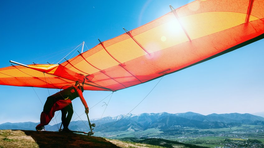 Man with hang-glider starting to fly from the hill top.