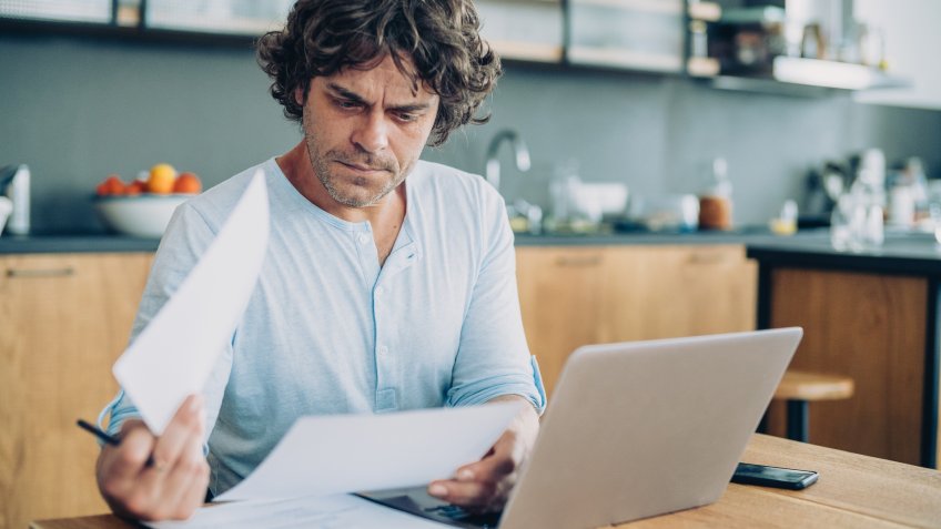 Man with smart phone and laptop working at living room.