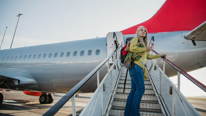 One mature woman is standing on the air-stair of her plane with her boarding pass and has turned round to give one last look to her home before she goes travelling.