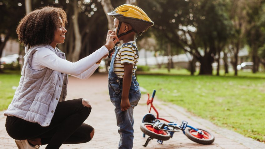 Mother helping son wearing helmet for cycling at park.