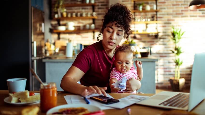 Close up of a mother using a phone with her daughter while having breakfast and doing bills.