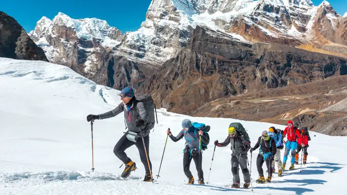 Adventurous People of variety of Age Origin and Ethnicity making Climb in high Altitude Mountains walking on Glacier with heavy Snow using trekking Poles and other Gear.