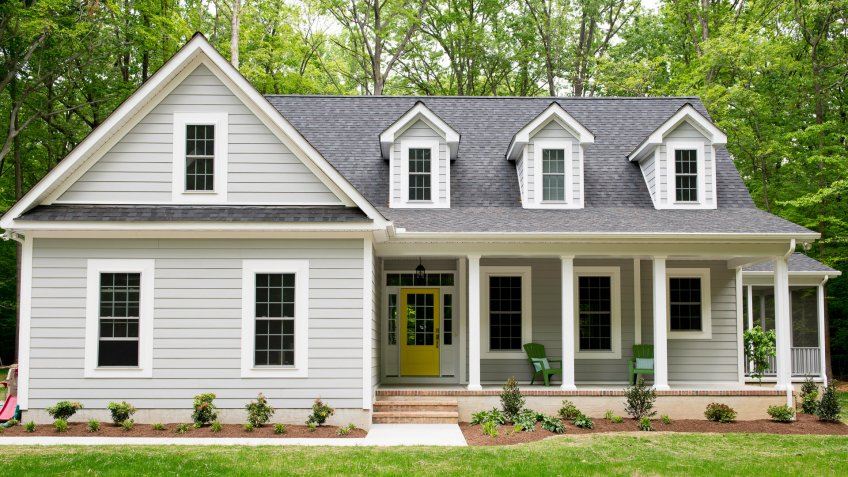 Exterior of a new Cape Cod styled suburban house with recently planted shrubs and grass.