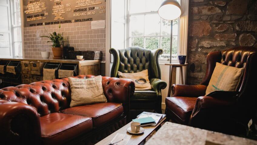 Empty interior of a small cafe, there is a seating area with leather sofas and a wooden table.