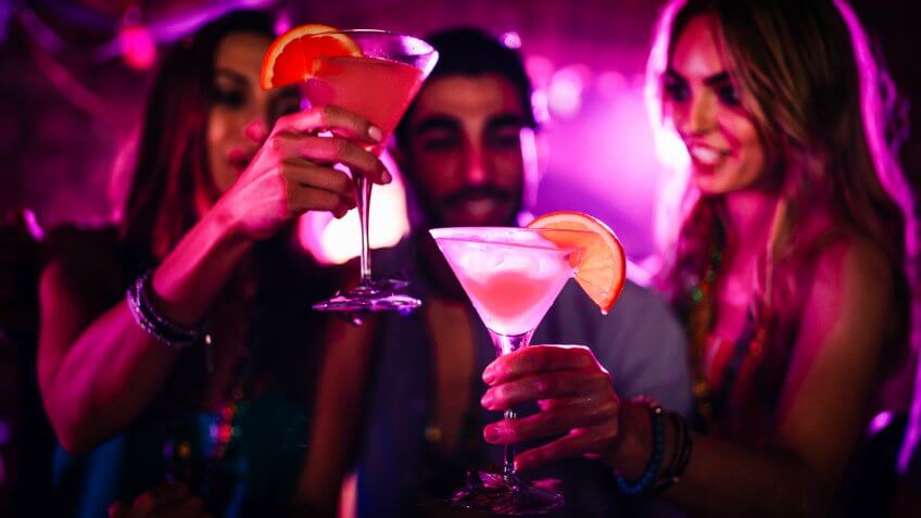 Young friends having fun and toasting with cocktails at night club Mardi Gras party.