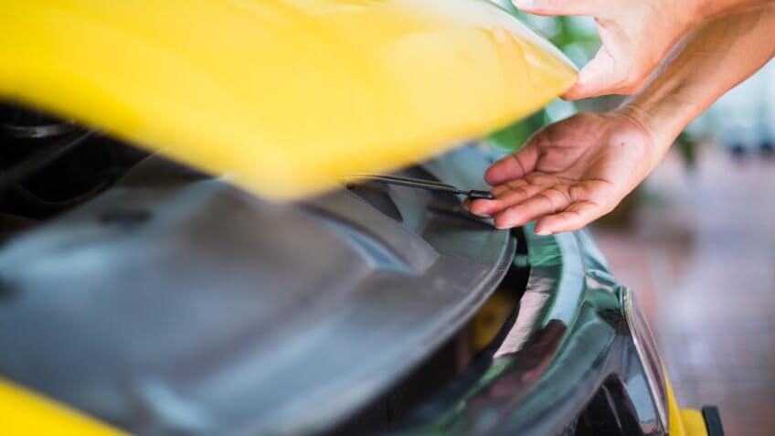 The man opened the hood of yellow car and looking for a malfunction.