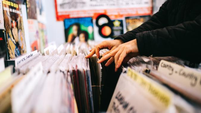 An unrecognisable male customer searches through and selects a second hand vinyl record from a shelf in a record store, hands only, horizontal composition.