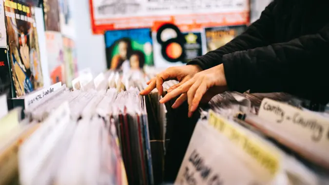 An unrecognisable male customer searches through and selects a second hand vinyl record from a shelf in a record store, hands only, horizontal composition.