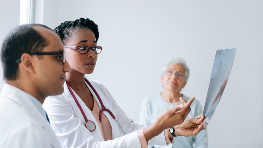 Two doctors holding and looking at an x-ray in front of a senior female patient.