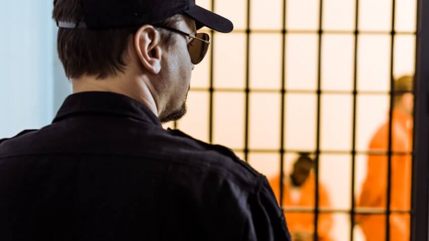 rear view of prison officer standing near prison cell with criminals.