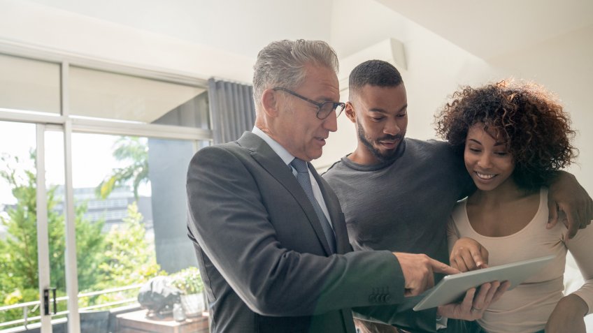 Real estate agent showing a property to a happy African American couple using a tablet computer â lifestyle concepts.