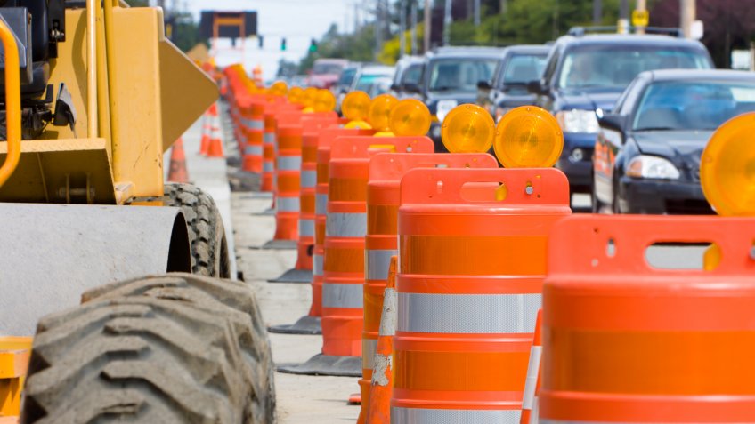 A row of bright Orange construction barriers separate construction from the busy traffic.
