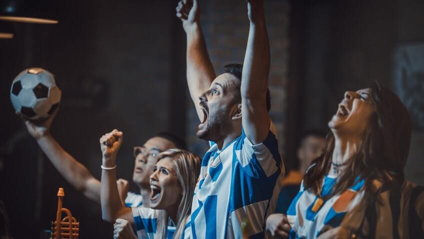 Young cheerful soccer fans celebrating victory of their team in a bar.