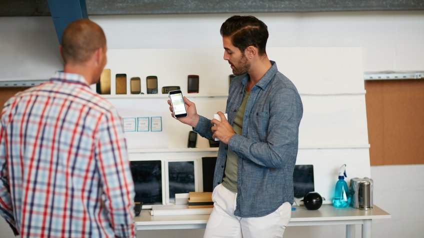 Shot of a young man showing his coworker something on a mobile phone.