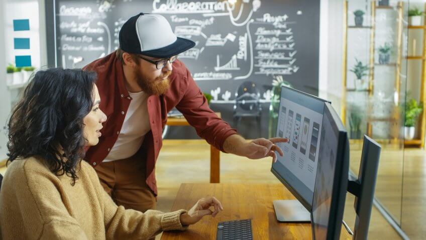 Beautiful Woman Developer Works on Her Personal Computer Designing Mobile Gaming App, She Talks with Male Programer.