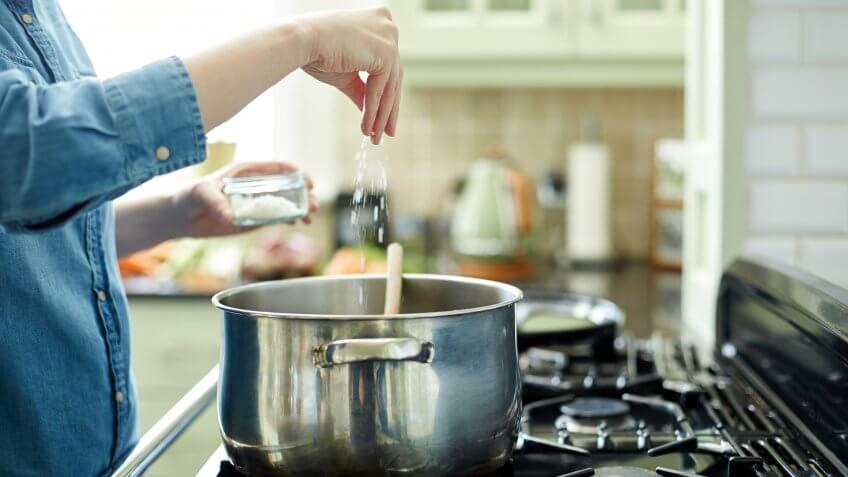 Midsection image of woman adding salt in cooking pot.