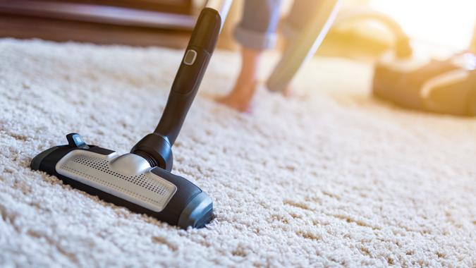 Young woman using a vacuum cleaner while cleaning carpet in the house.