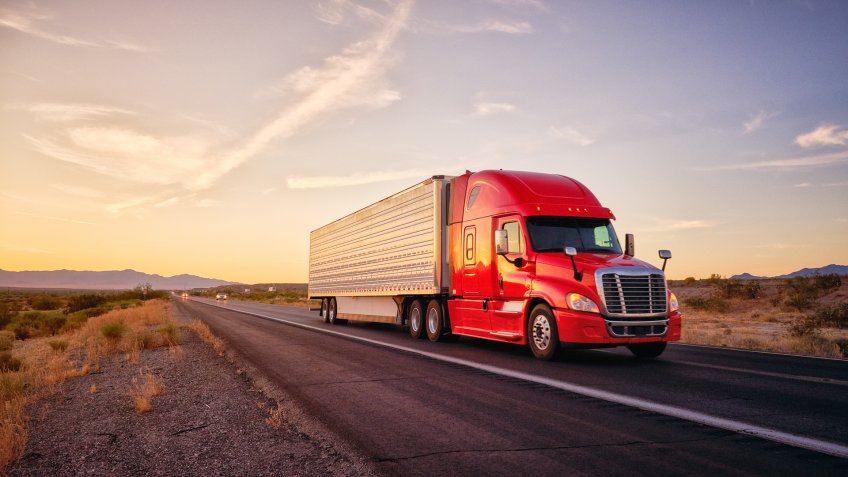 Large semi truck hauling freight on the open highway in the western USA under an evening sky.