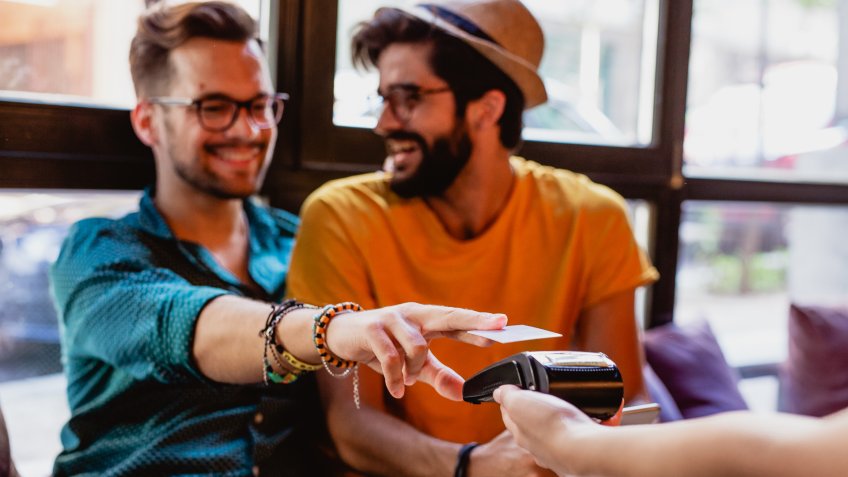 Two gay men pay in bar with credit card.