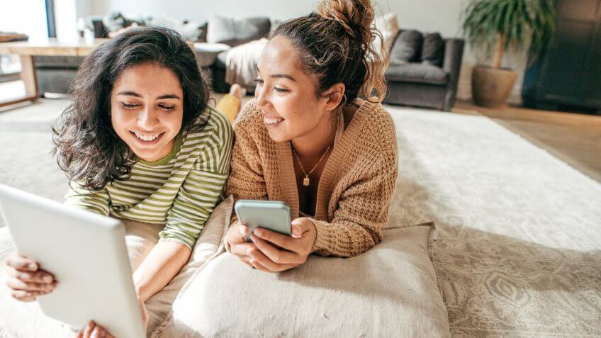 Two female students with digital tablet and cellphone at home.