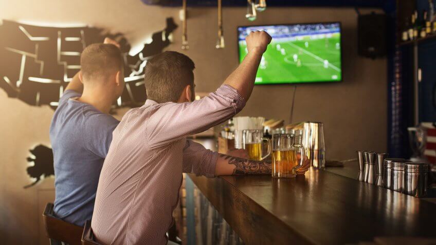 Two friends watching football game and drinking beer at the pub.