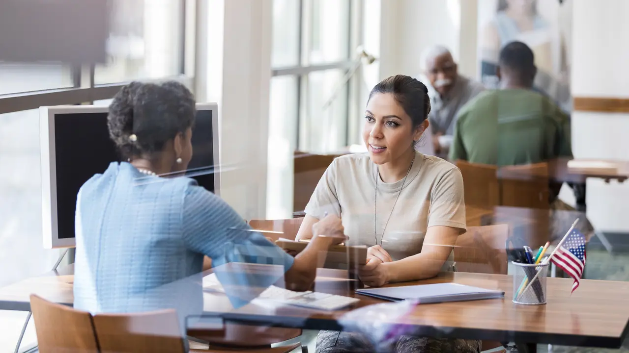 An African American bank officer assists a Hispanic female soldier in understanding a loan application form.