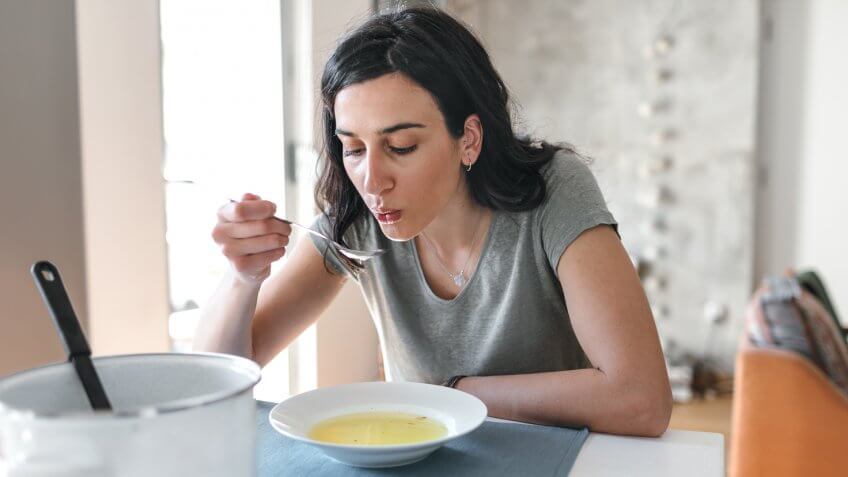 Young woman sick at home eating soup.