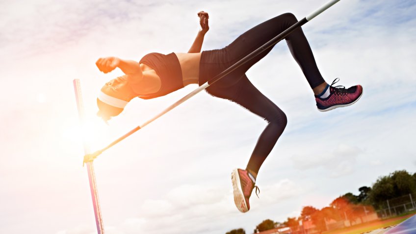 Shot of a young woman in mid air doing a high jump on a sports field.