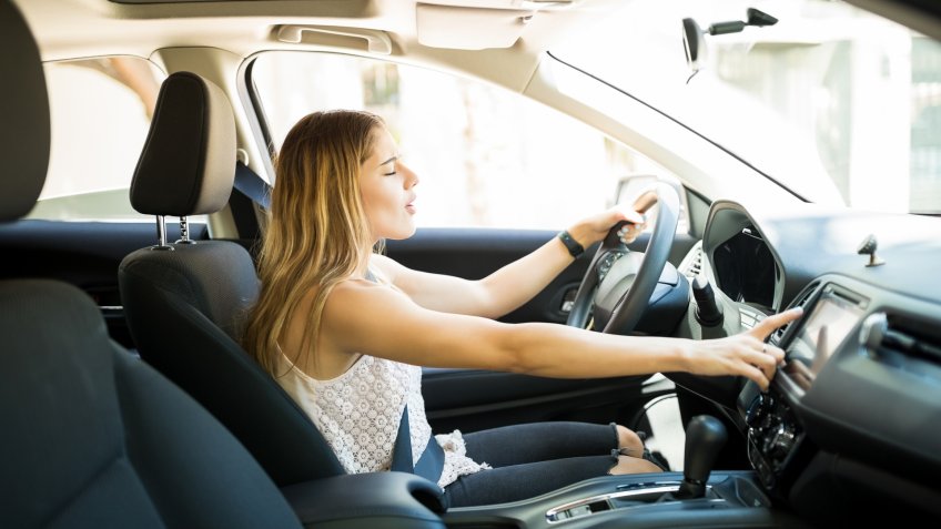 Beautiful young woman using infotainment on dashboard of car while driving.