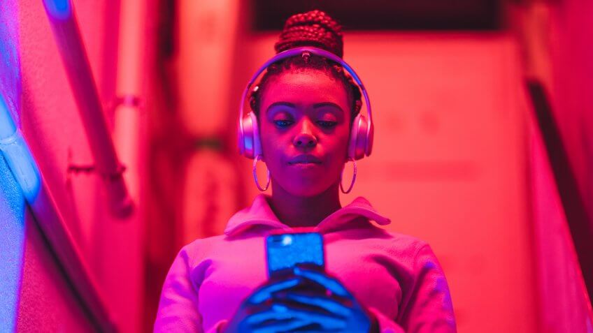 A portrait of a young black woman while she is listening to music under neon lights.