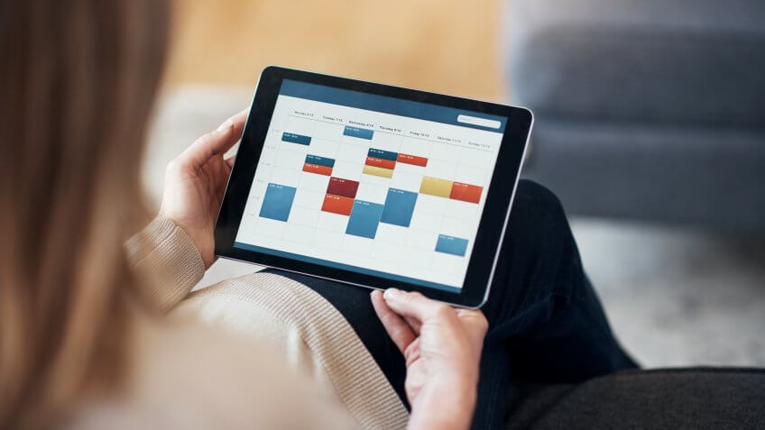 Cropped shot of an unrecognizable woman sitting and viewing a timetable on a tablet in her living room.