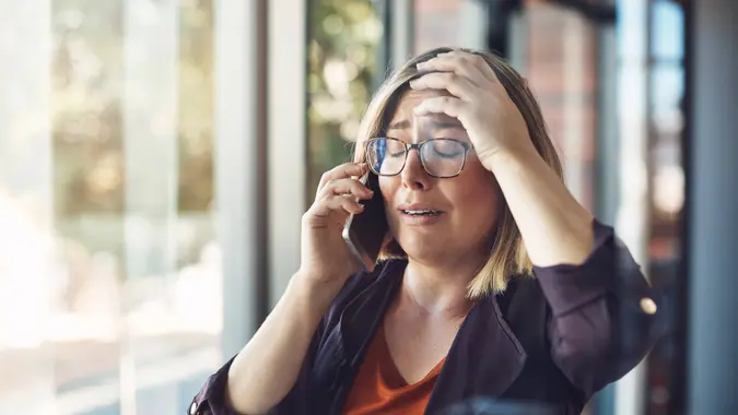 Shot of a young woman looking distraught while talking on a mobile phone in a modern office.