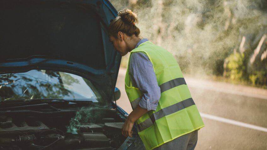 Young woman standing by opened car hood on the road.