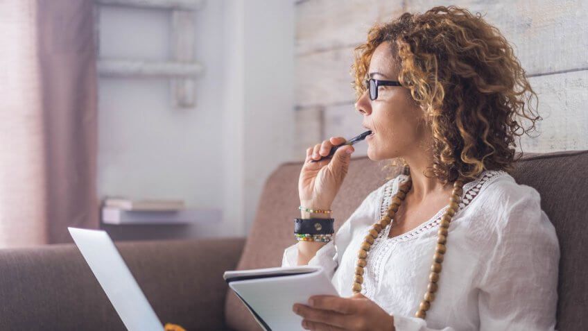 beautiful woman think and write notes on paper working on a laptop freedom from office at home.