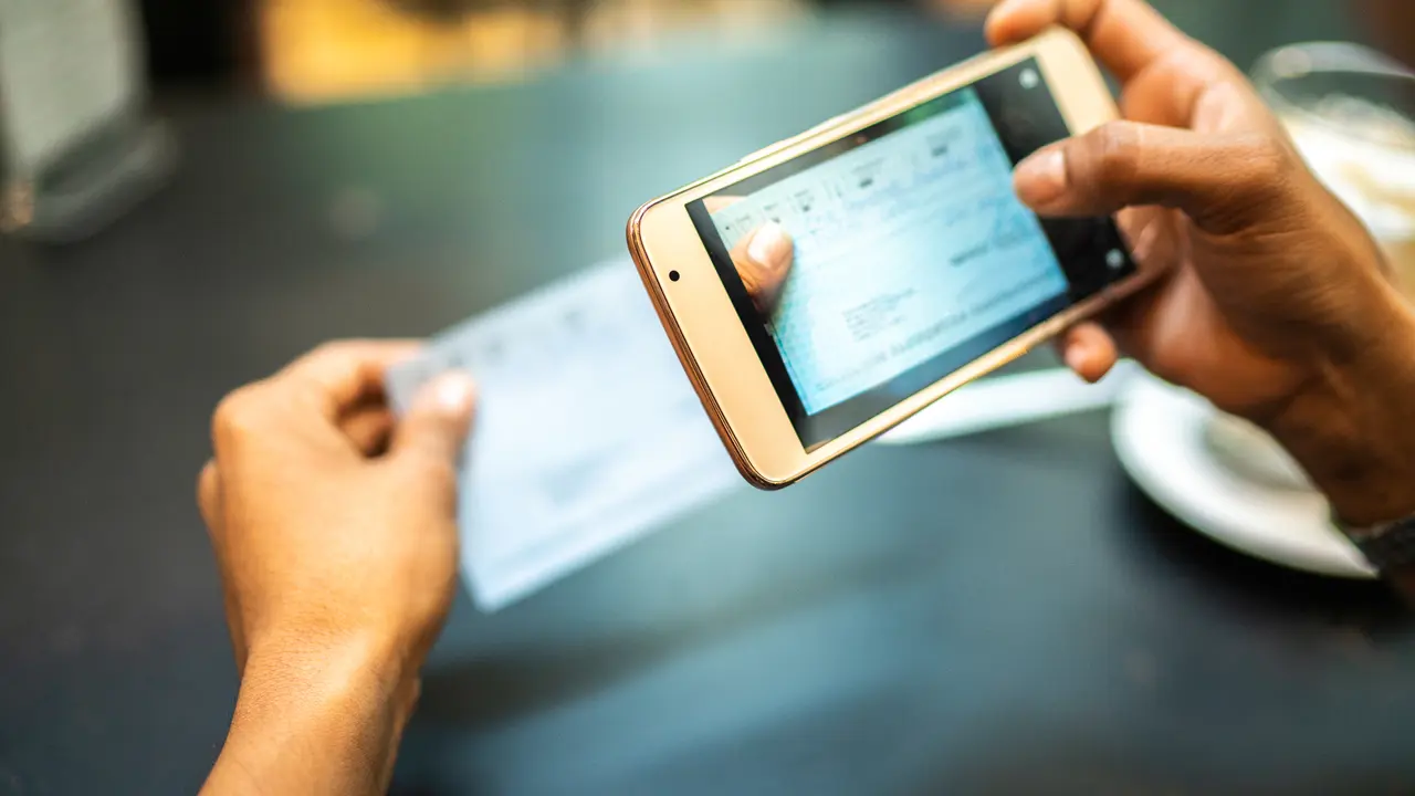 Young woman depositing check by phone in the cafe.