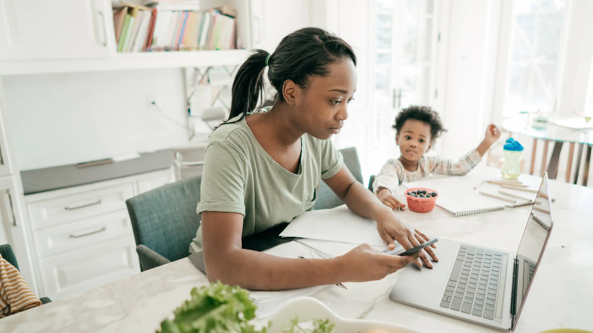 一位母亲正在使用她的笔记本电脑，她的孩子盯着她在做什么。
